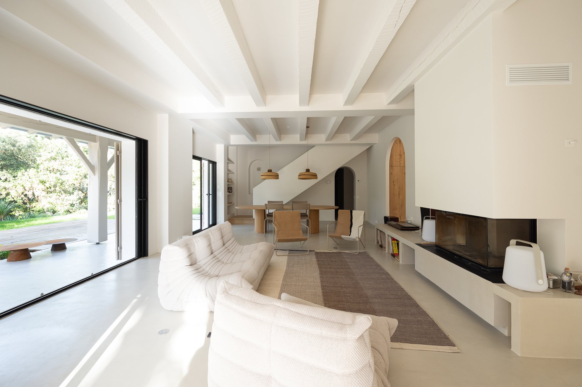Séjour aux poutres blanches ouvert sur la terrasse par une grande baie coulissante, villa du Bassin d'Arcachon photographiée par Maison Òstra