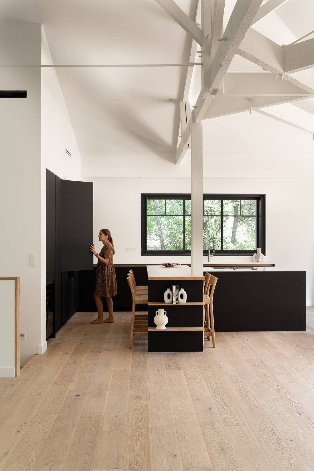 Cuisine noire sur mesure sous une charpente peinte en blanc, réalisation photographiée par Maison Òstra